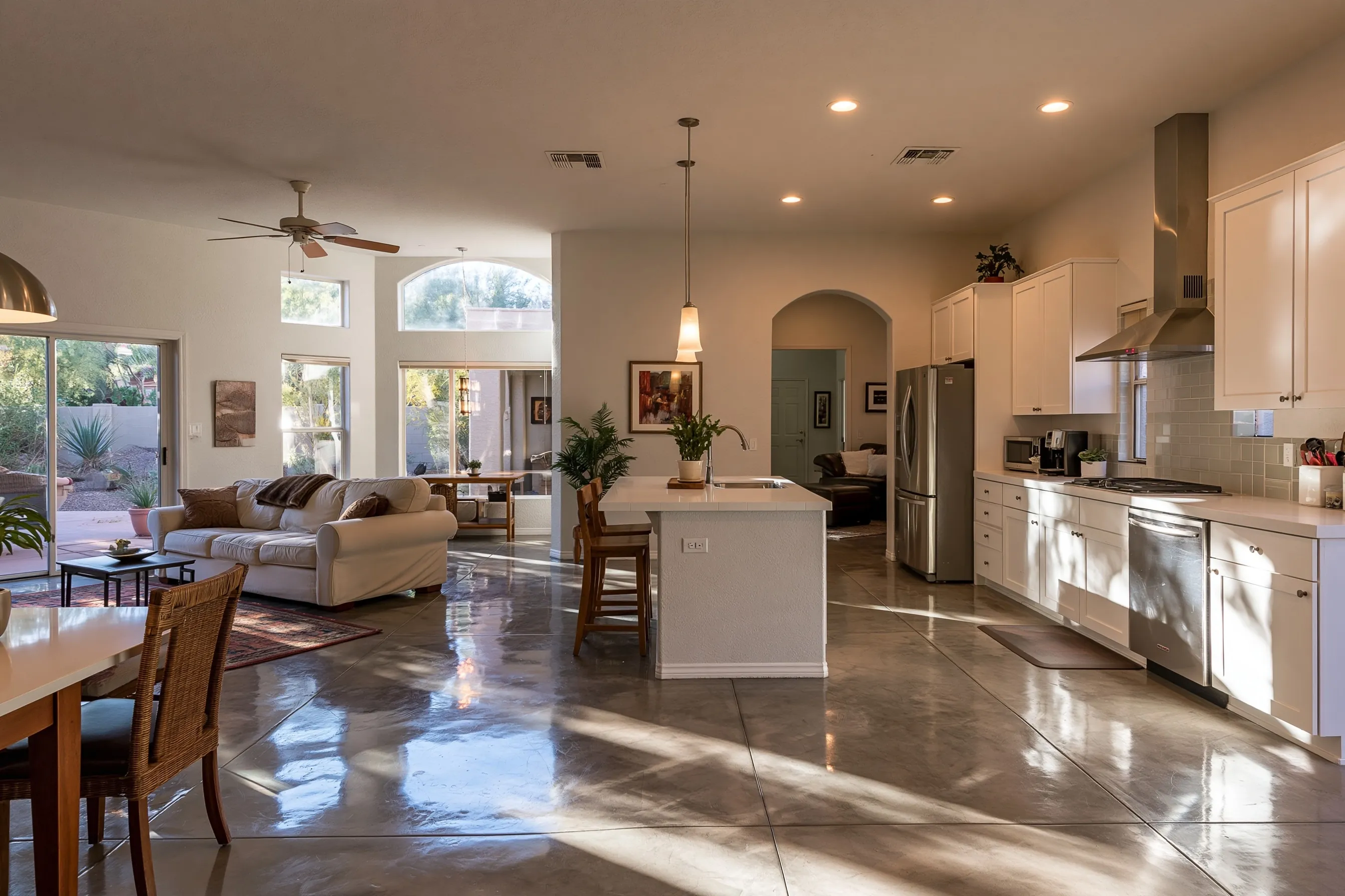 Open kitchen and family room with a mottled warm gray-brown polished concrete floor, white cabinets, an island and an arched doorway